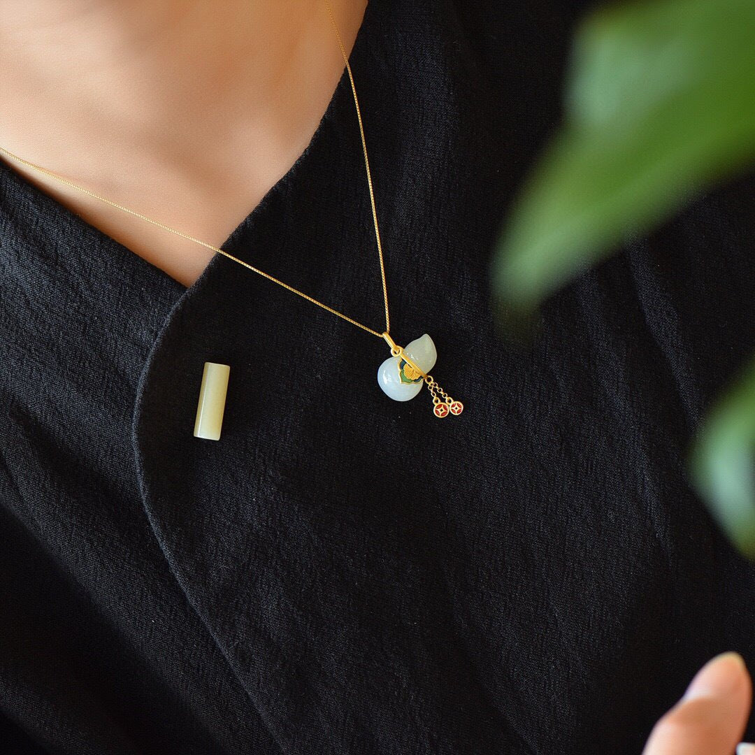 Woman wearing a dainty white jade gourd pendant necklace with gold accents.