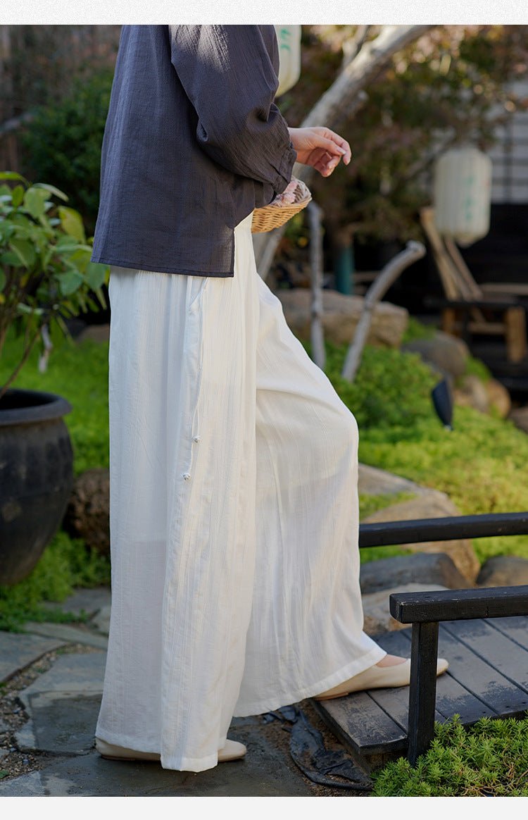 Model in soft cotton trousers holding a bamboo fan – stillness and breath in a summer morning