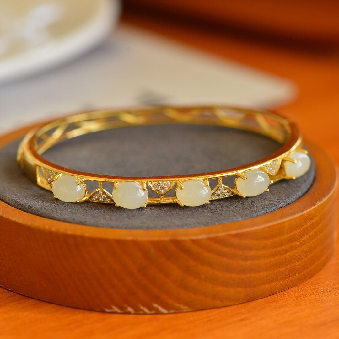 Stylish gold and jade bracelet with repeating oval white jade patterns, displayed beside a teacup.