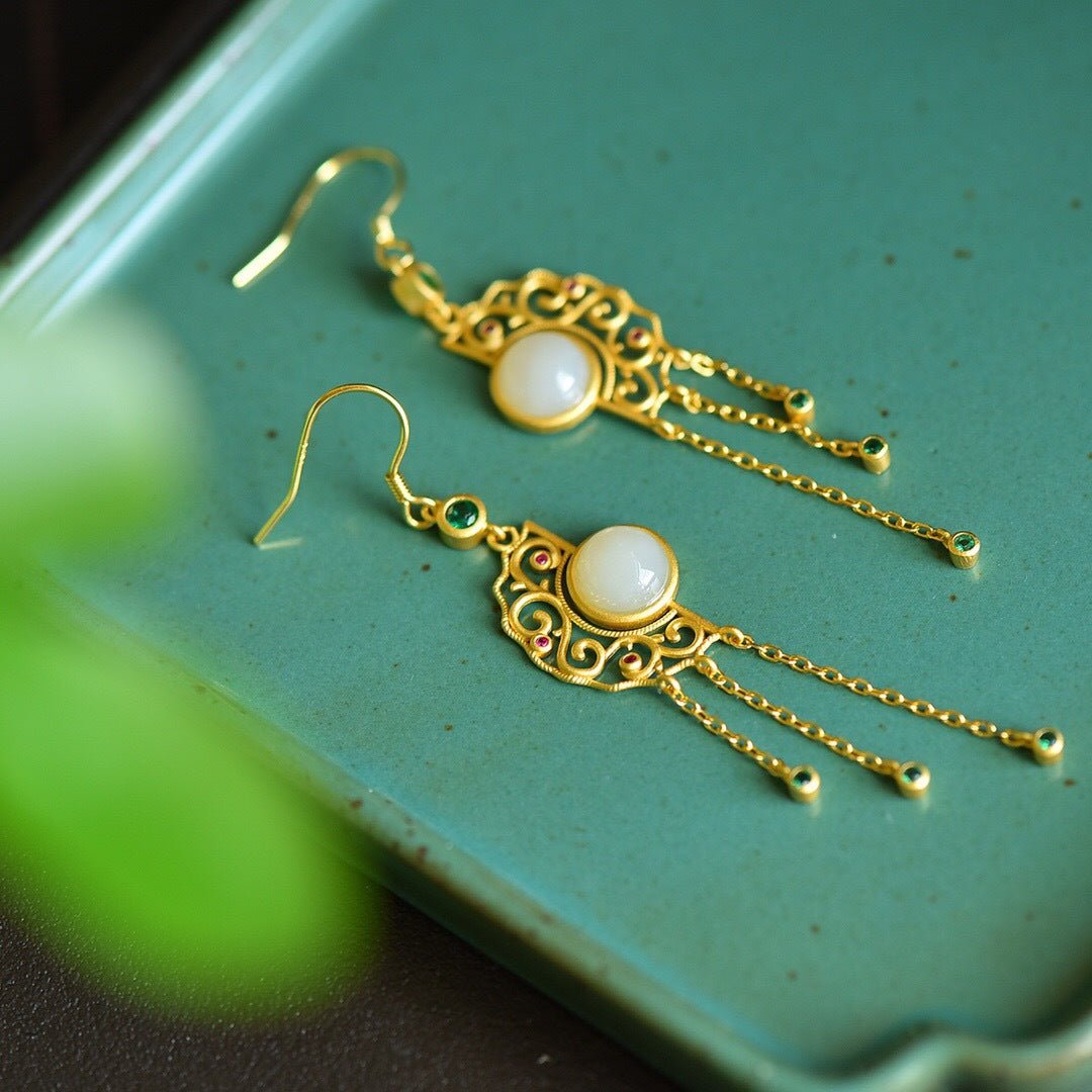 Close-up of jade and gold tassel earrings on teal surface – rich color contrast and delicate craftsmanship