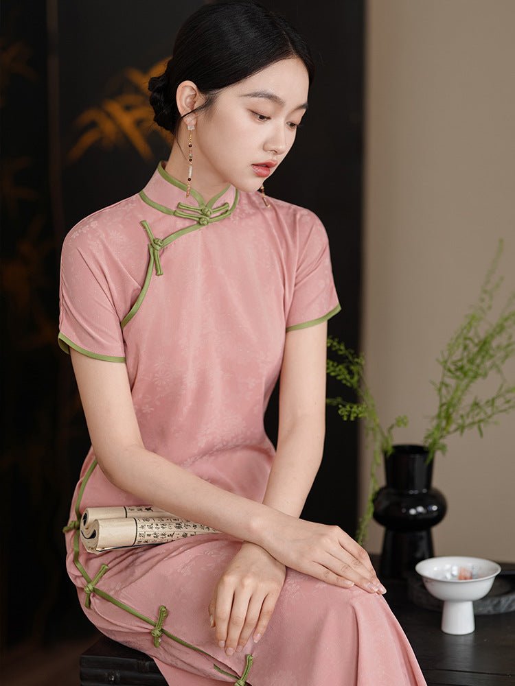 Elegant lady in a pink cheongsam sitting on a wooden chair, hands folded on her lap.