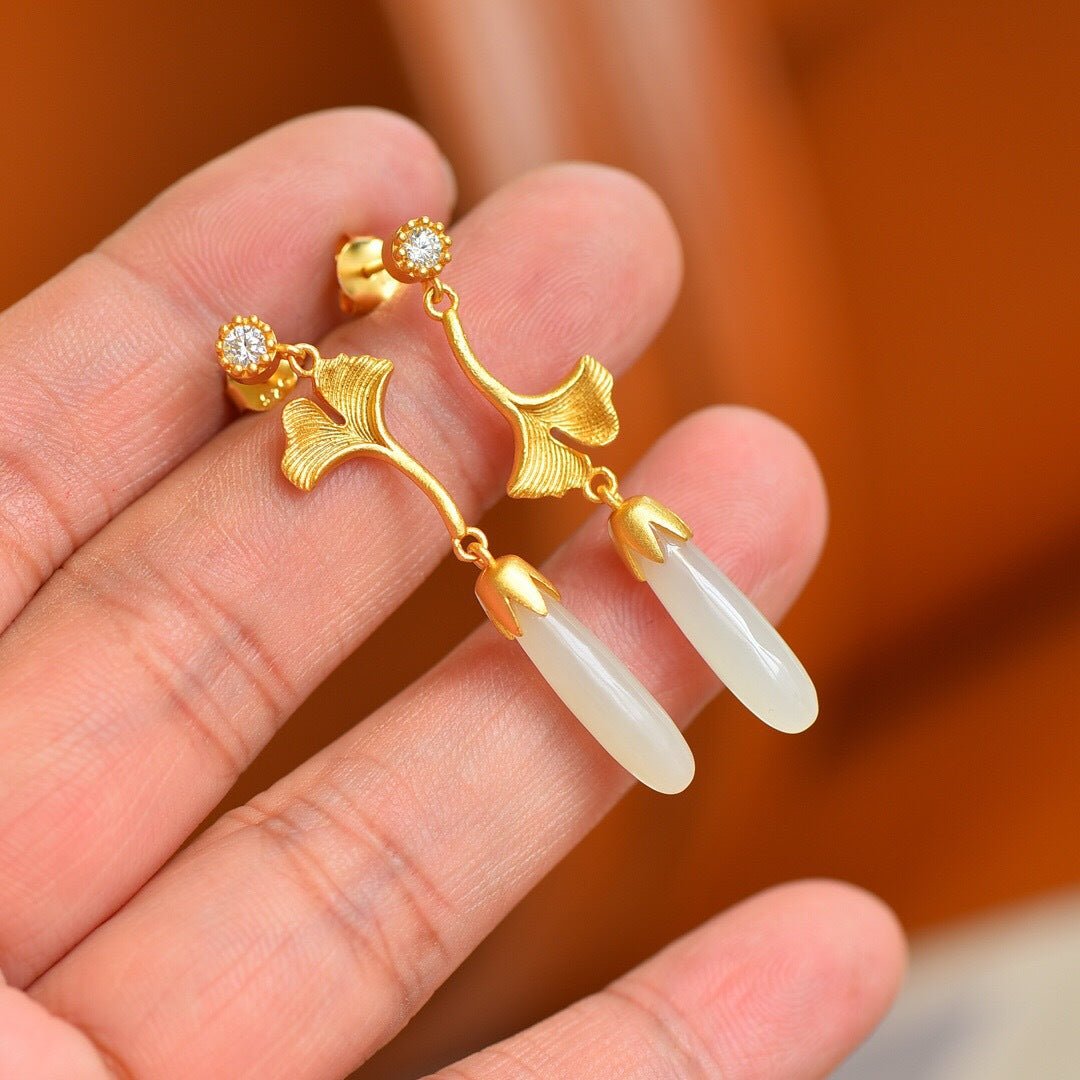 Hand holding jade and gold earrings – light catching the curved leaves, crafted with calm precision