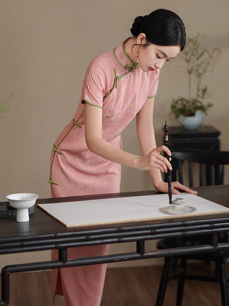 Woman in a blush pink modern qipao leaning over a tea table, with a calm and focused expression.
