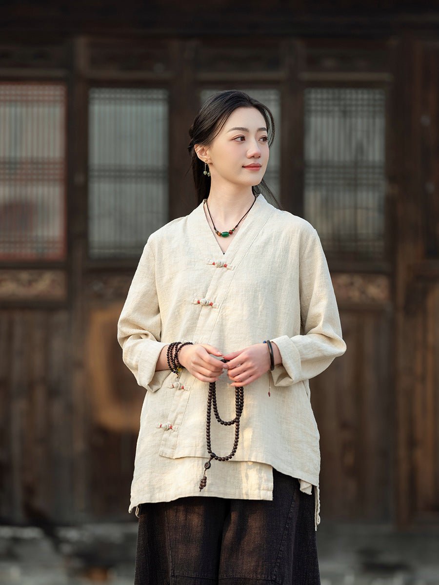 Woman in a white linen top with Chinese knot buttons, standing calmly in front of a traditional wooden building.