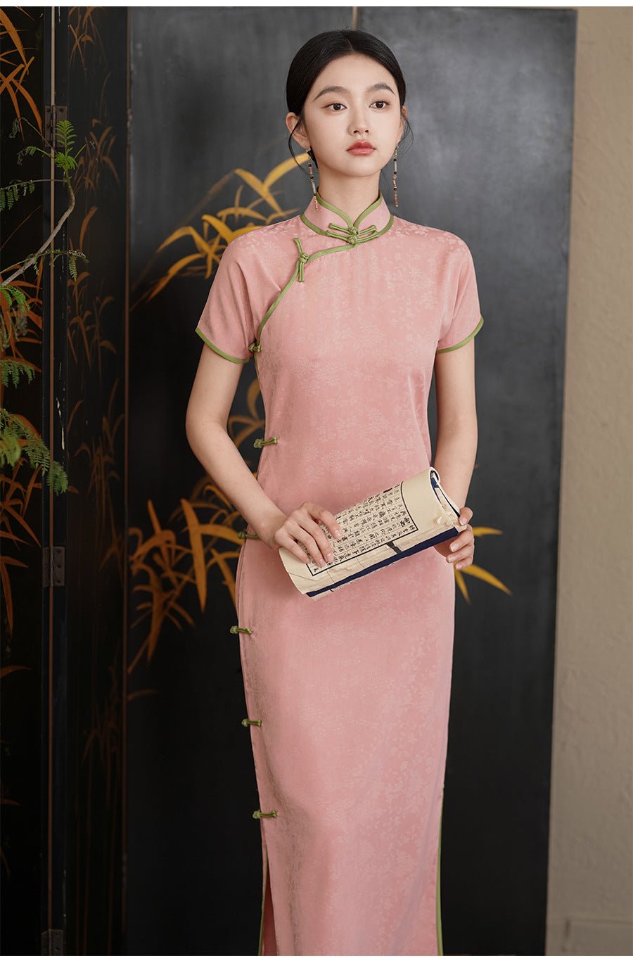 Woman standing gracefully in a soft pink qipao dress with floral embroidery and mandarin collar.
