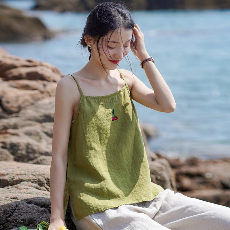 Soft flax cami in a quiet seaside moment – model seated on rocks, calm and thoughtful expression