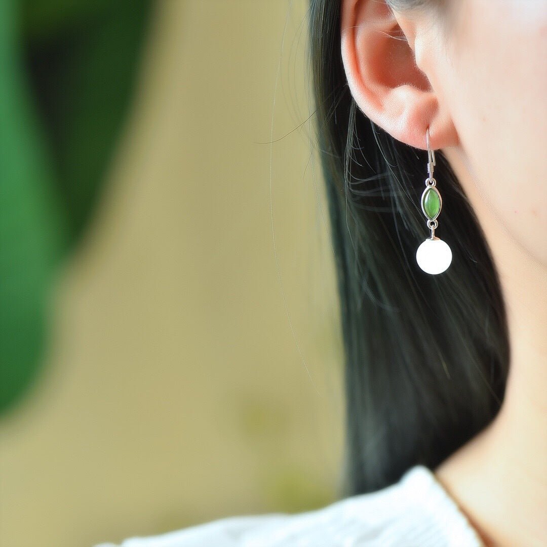 Elegant white jade drop earrings with green accents, worn by model with sleek hair.