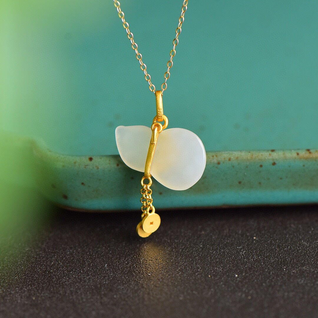 Gold chain necklace with white jade gourd pendant, styled against green and black backdrop.