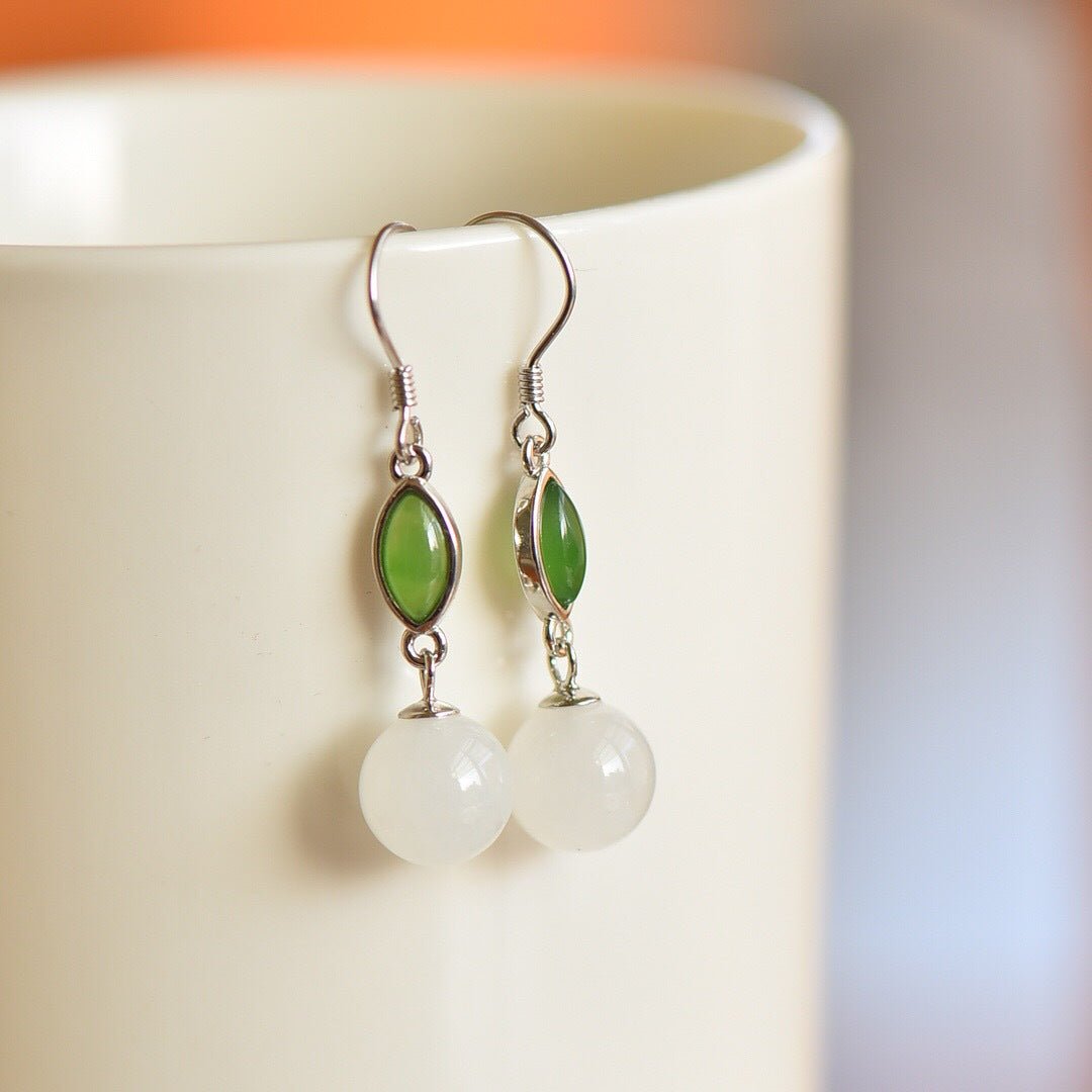 Delicate green and white jade dangle earrings displayed on a minimalist ceramic holder.