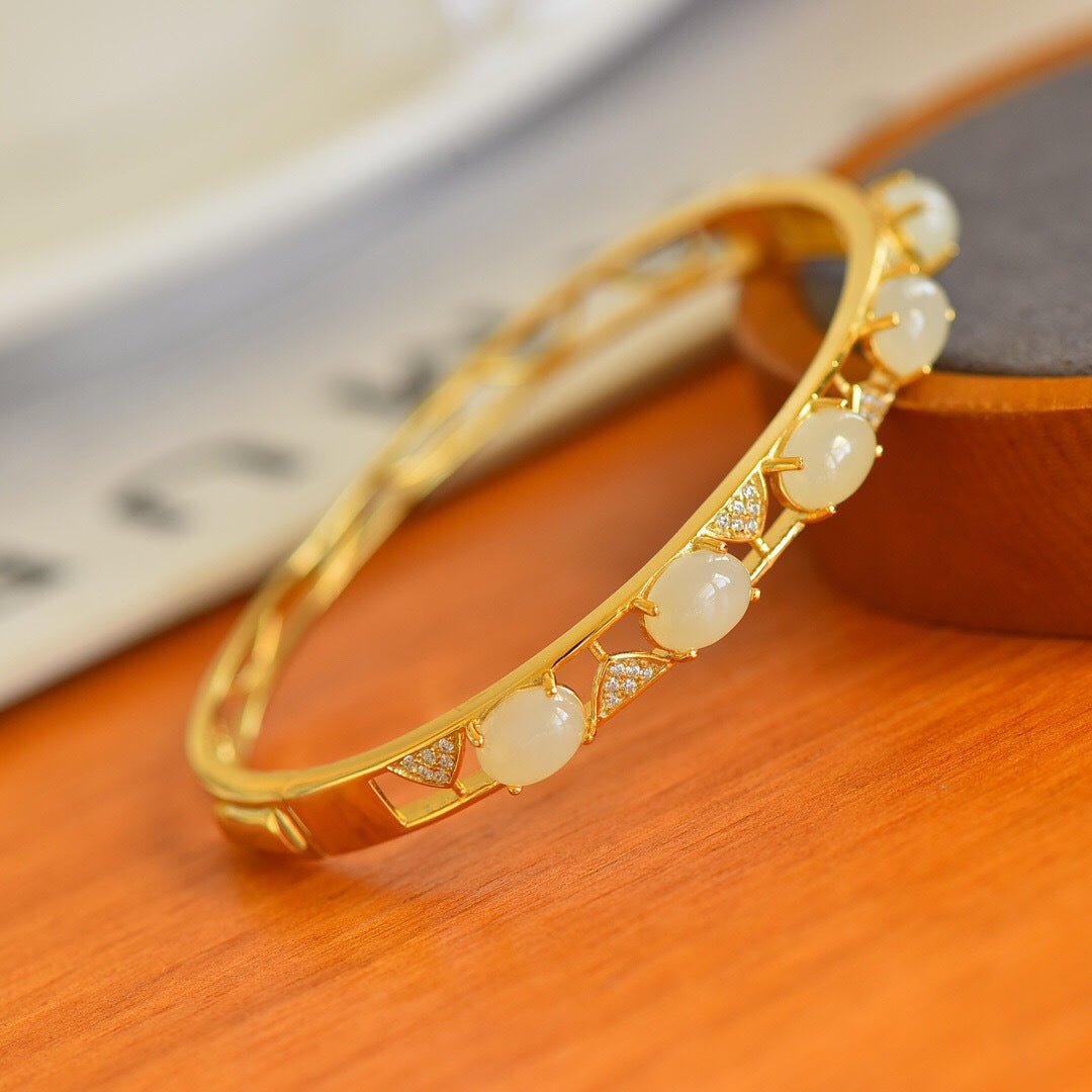 Close-up of a circular gold bangle featuring symmetrical white jade inlays, placed on an orange wood surface.
