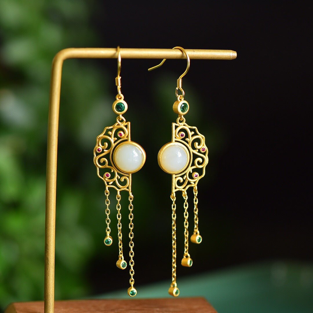 White Hetian jade earrings with gold tassels hanging on a stand – graceful symmetry and luminous detail
