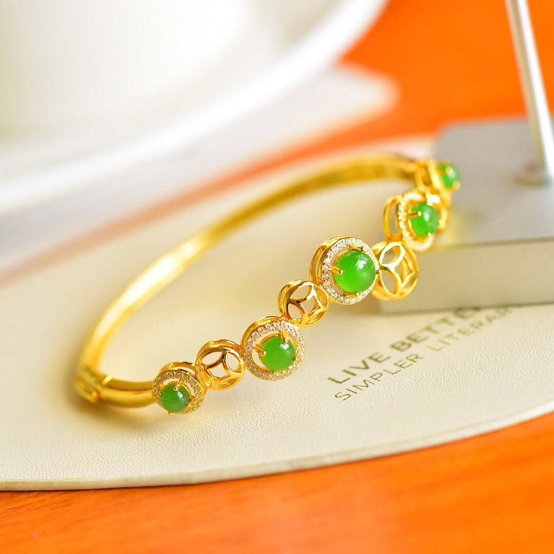 Gold bracelet with five round green jade stones, styled on white plate and orange background.