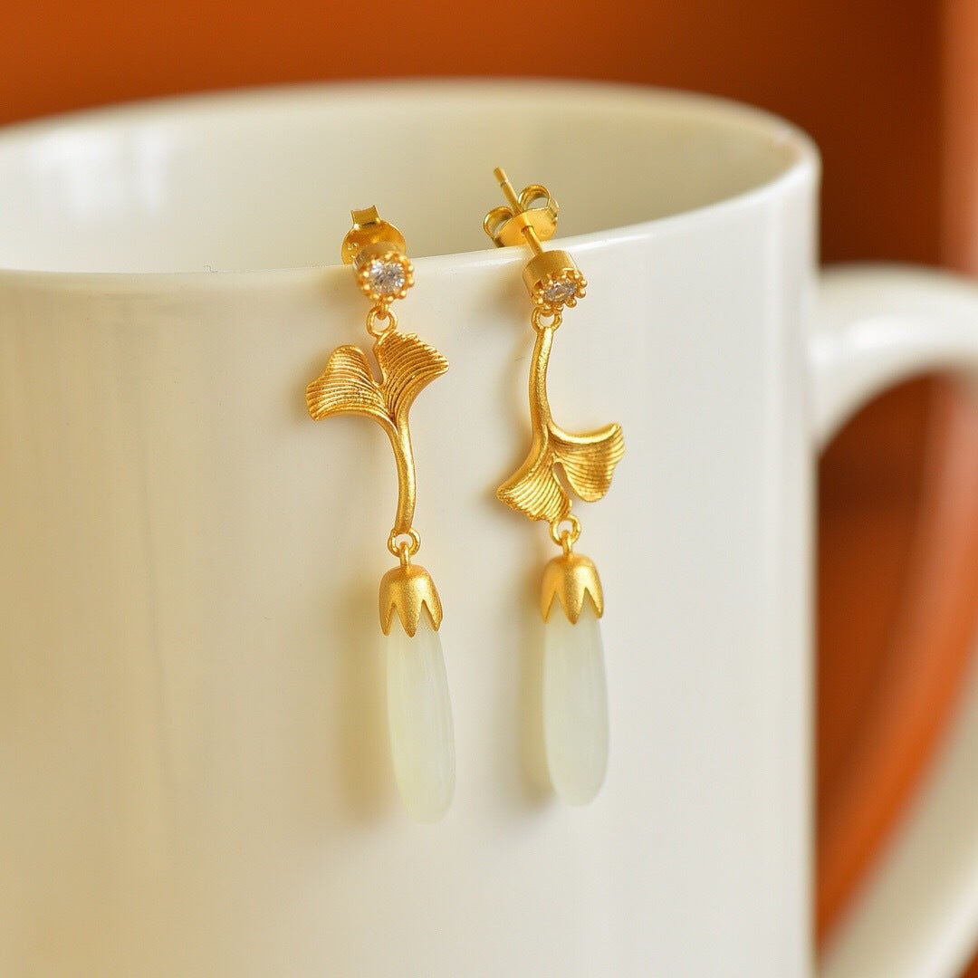 White jade earrings hanging on a ceramic cup – golden ginkgo leaves shining in warm light