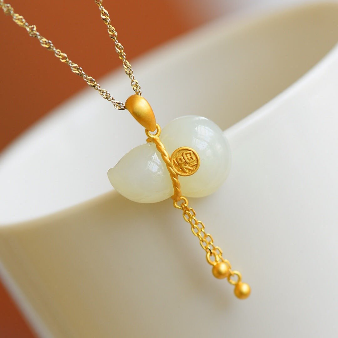 White Hetian jade gourd pendant with delicate gold tassel resting on smooth porcelain – warm-toned still life