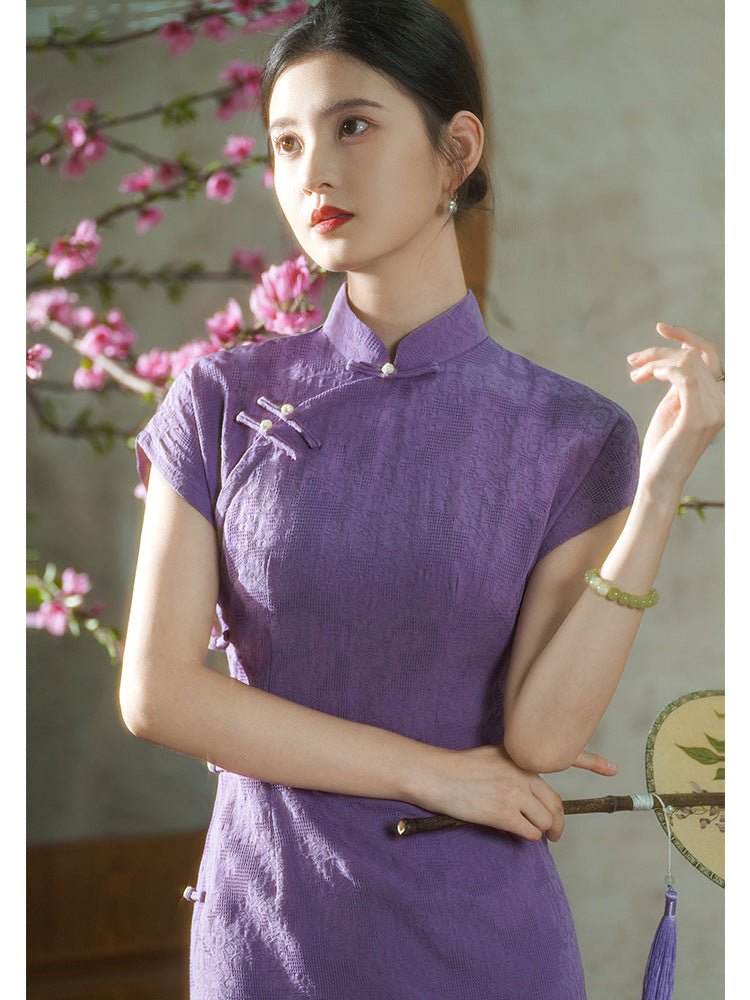 Graceful woman in a purple qipao standing beside blooming peach blossoms, gently turning her head.