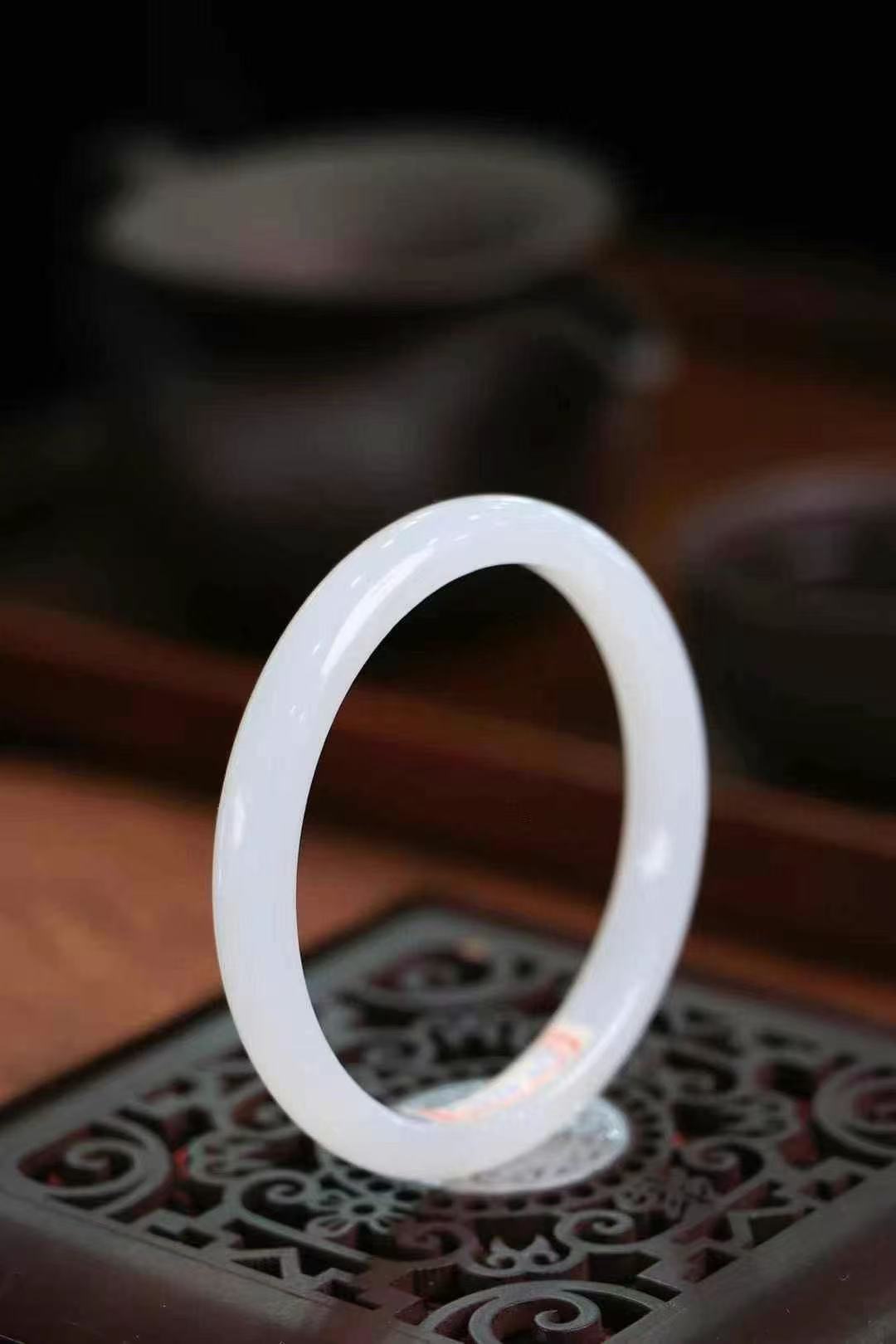Delicate white jade bracelet placed on a dark wooden table, calm and refined
