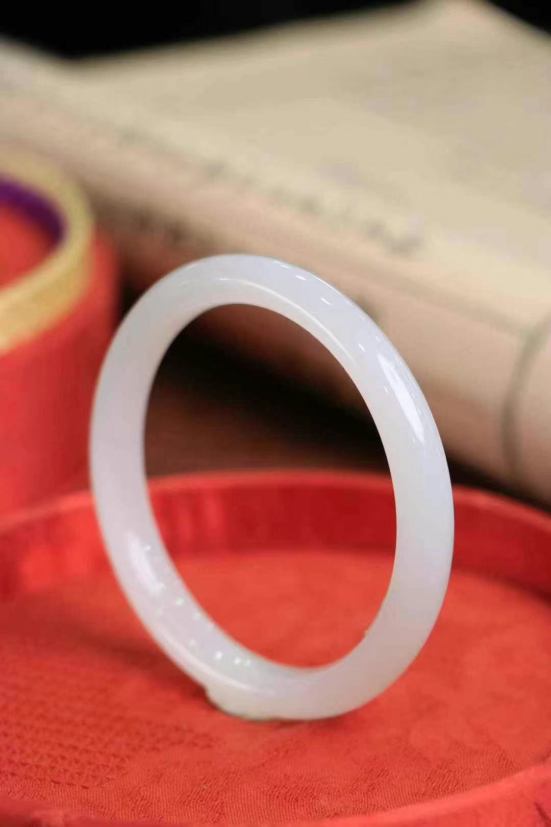 White jade bangle resting softly on red silk, with a warm, elegant glow