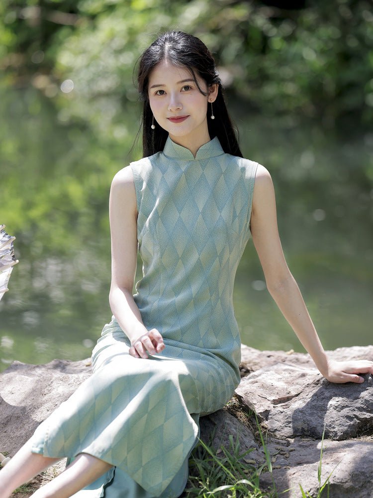 Woman in a sleeveless green qipao sitting by a rock in a serene garden, gazing into the distance.