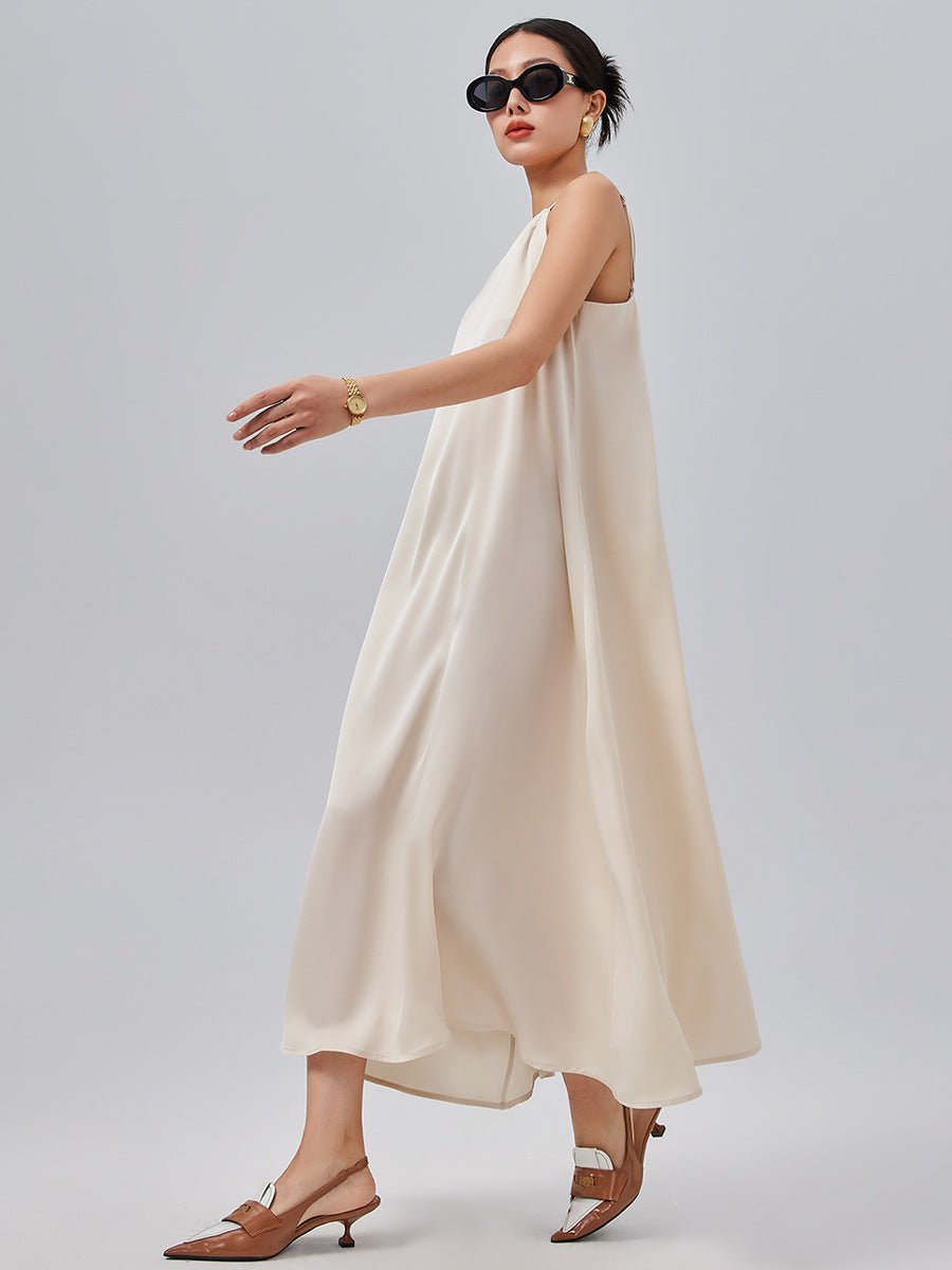 Woman walking in a flowy off-white spaghetti strap maxi dress with sunglasses and sandals.