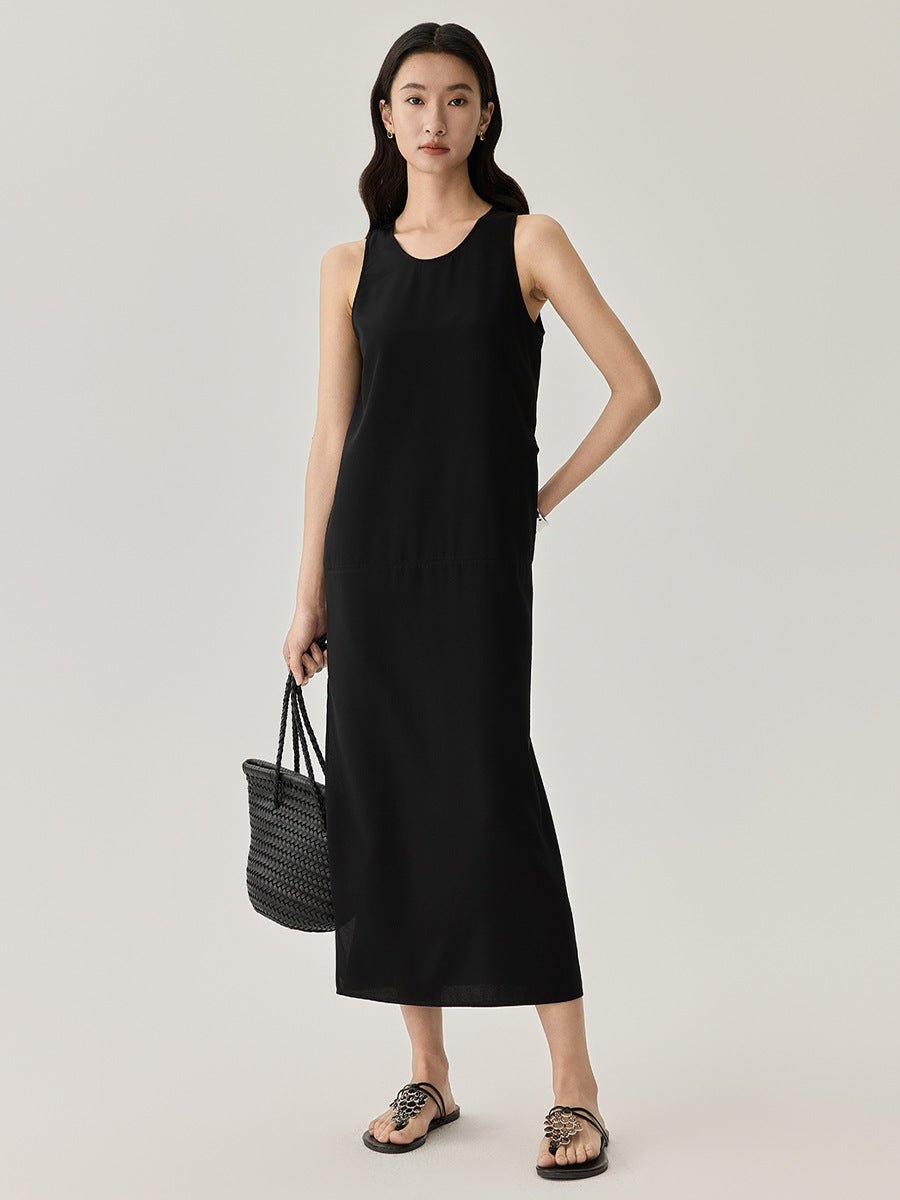 Woman wearing a sleeveless black midi dress with a minimalist silhouette, holding a black handbag.