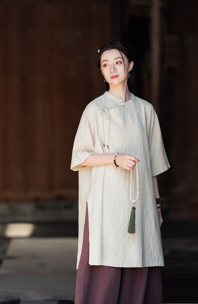 Woman in loose off-white linen outfit with mandarin collar, standing calmly by a wooden doorway.