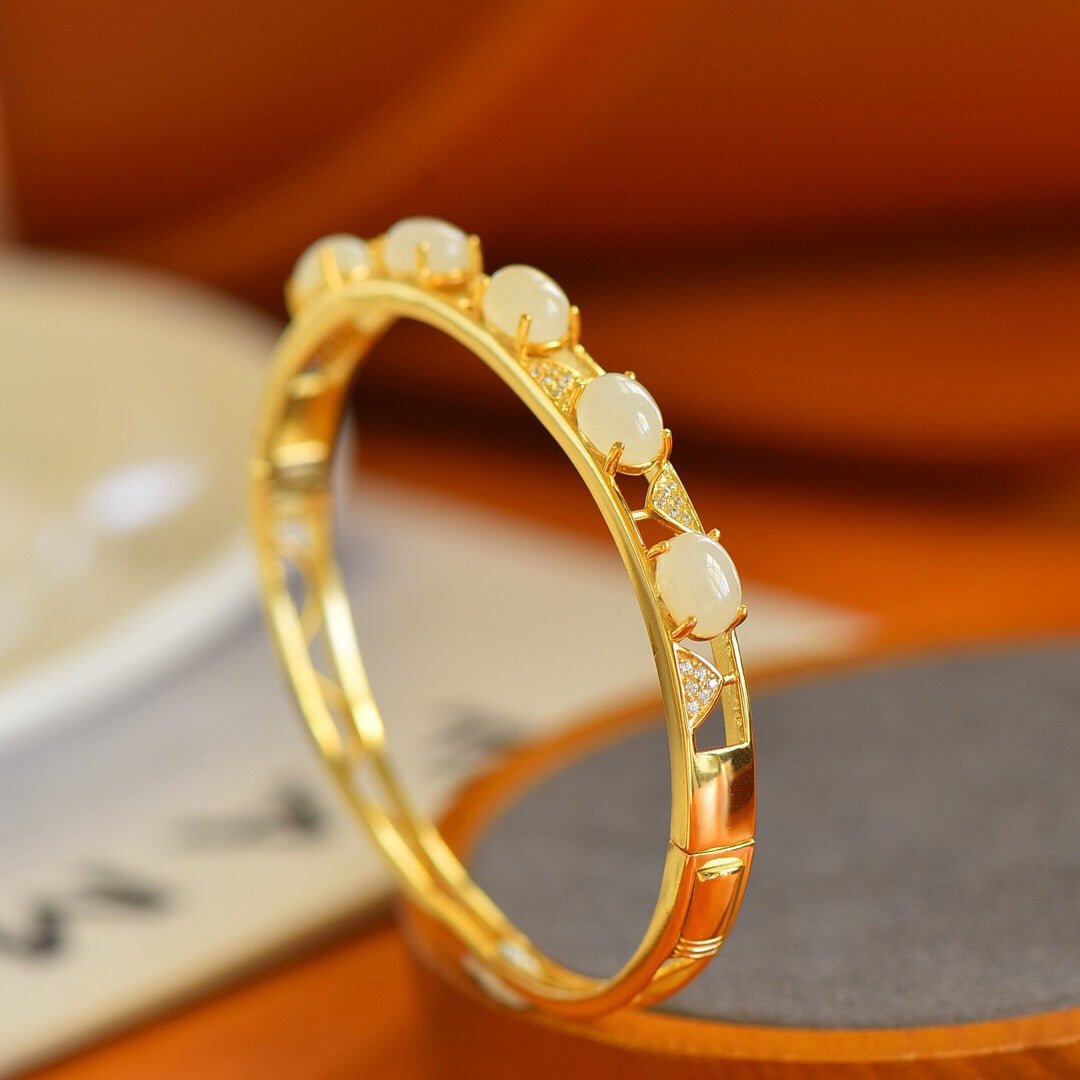 Golden bracelet with inlaid white jade pieces, resting on a soft grey cushion.